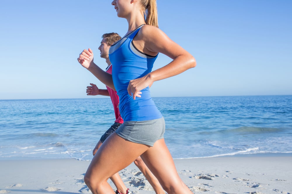 Happy couple running together beside the water at the beach